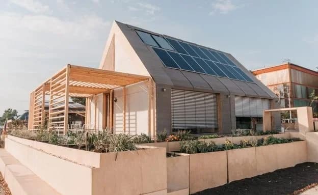 Fachada de la casa Barraca, con su cubierta fotovoltaica inclinada, pérgola de madera y jardineras.